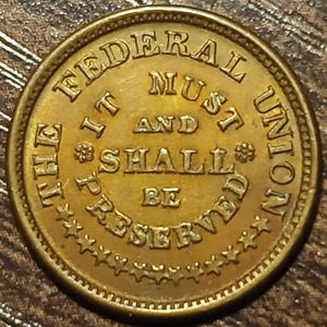 May include: A round, antique-looking bronze coin with the text "THE FEDERAL UNION IT MUST AND SHALL BE PRESERVED" encircling the edge. The coin has a detailed border with small stars.