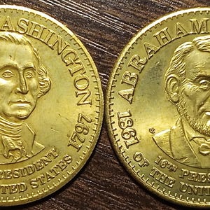 May include: Two gold-colored coins. One coin features George Washington, the first U.S. president, with the text "1789" and "1797". The other coin depicts Abraham Lincoln, the 16th president, with the text "1861" and "1865".