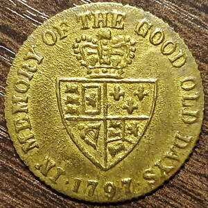 May include: A gold-colored coin with the text "MEMORY OF THE GOOD OLD DAYS" and the date "1797". The coin features a crown above a shield with various emblems.