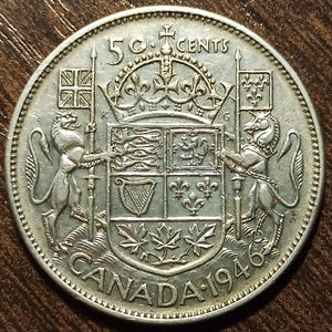 May include: A silver Canadian 50-cent coin from 1946 featuring the Canadian coat of arms with a lion and a unicorn on either side.