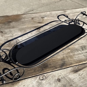 May include: Black metal serving tray with a long, oval shape and decorative scrollwork. The tray has a solid black center and handles at each end. The tray is approximately 28 inches long.