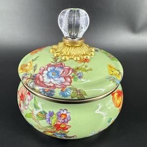 以下が含まれることがあります： カラフルな花柄で飾られた、蓋付きの装飾的な丸い緑色のセラミックジャー。蓋は透明なファセットノブと金色のフィリグリーベースで覆われています。ジャーのデザインは、バラ、蝶、その他の花を特徴としています。