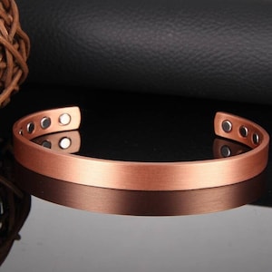 Könnte beinhalten: Ein kupfernes Magnetarmband mit gebürsteter Oberfläche. Das Armband hat fünf Magnete auf jeder Seite.