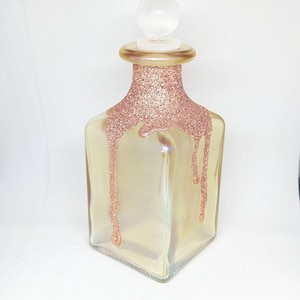May include: A clear glass bottle with a round glass stopper. The bottle is decorated with gold glitter that drips down the sides.