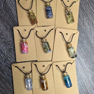 May include: Ten necklaces with small glass bottles filled with various colorful glitter, dried flowers, and other decorative elements. Each necklace is displayed on a brown card with a black cord.