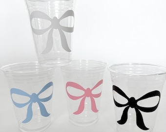 May include: Four clear plastic cups with a bow design on the front. The bows are in white, light blue, pink, and black.