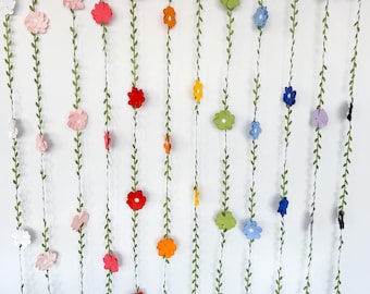 May include: A garland of green paper leaves with colorful paper flowers in shades of pink, red, orange, yellow, green, blue, and black.