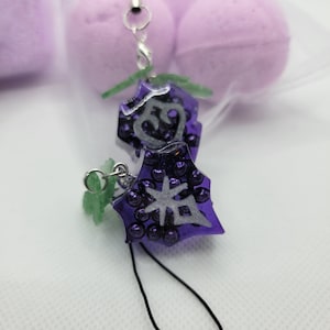 May include: Close-up of two purple charm pendants with silver accents and black cords. The pendants have a star and heart design, surrounded by small purple beads. Green leaf accents are attached to the top of the pendants.