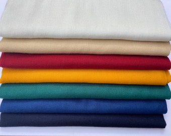 May include: A stack of folded fabric samples in various colors. The colors include cream, tan, red, yellow, teal, blue, and navy. The fabric appears to be a tightly woven canvas or similar material.