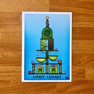 May include: A green cat tree shaped like a Christmas tree with a star on top. The cat tree has multiple levels with cat toys and a cat bed. The text "Merry Catmas!" is at the bottom of the image.