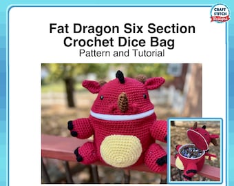 Puede incluir: Una bolsa de dados de crochet con forma de dragón roja con una cremallera blanca y una barriga amarilla. La bolsa está abierta para revelar los dados en el interior. La bolsa está sentada en una barandilla de madera.
