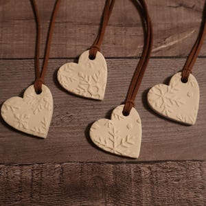 May include: Four white ceramic heart-shaped ornaments with snowflake designs, each hanging from a brown cord.