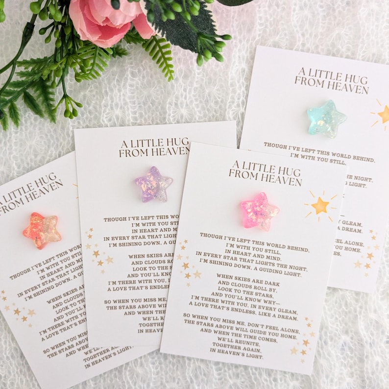 May include: Four white cards with a pink, purple, and blue star on each. The cards have the text "A Little Hug From Heaven" and a poem about being with you still.