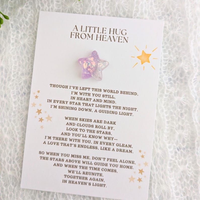 May include: A white card with gold lettering that reads "A Little Hug From Heaven". The card features a purple star with glitter and a yellow star. The card includes a poem about a loved one who has passed away.