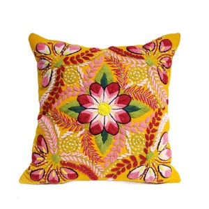 May include: A yellow throw pillow with a colorful embroidered floral design. The pillow features pink, red, green, and white flowers with intricate details.