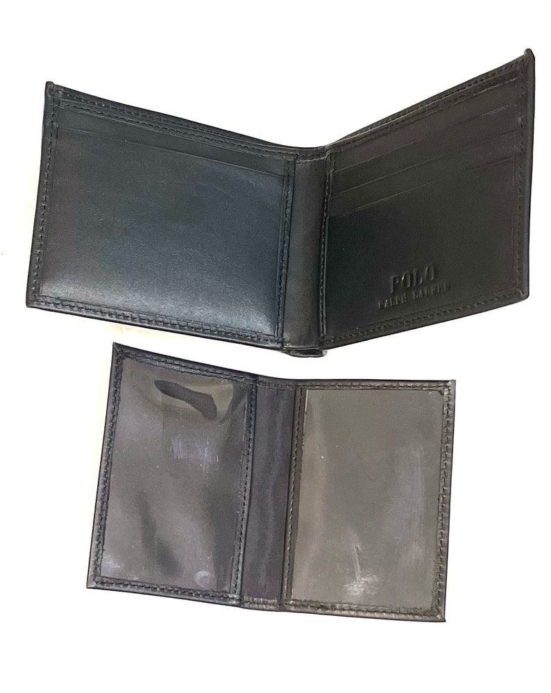 May include: Black leather bi-fold wallet with a Polo Ralph Lauren logo on the inside. The wallet has multiple card slots and a clear plastic ID window.
