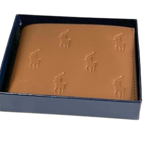 Op de afbeelding: Een bruine leren portemonnee in een blauwe doos. De portemonnee heeft een herhalend patroon van een polospeler op een paard.