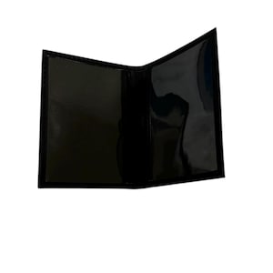 May include: A black, open, bi-fold wallet with a glossy finish. The interior features clear plastic sleeves for holding cards or identification. The wallet is empty and appears to be made of a smooth, possibly leather-like material.