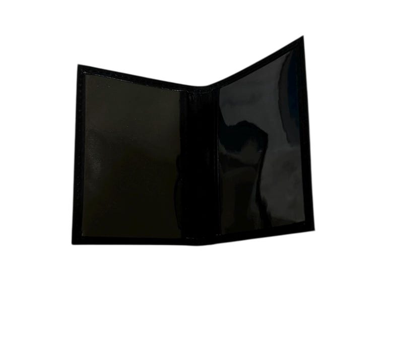 May include: A black, open, bi-fold wallet with a glossy finish. The interior features clear plastic sleeves for holding cards or identification. The wallet is empty and appears to be made of a smooth, possibly leather-like material.