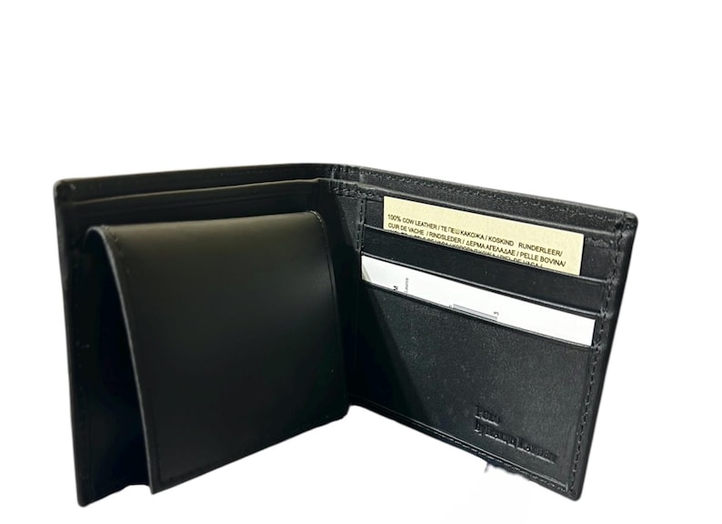 May include: Black leather wallet, open to display multiple compartments. The wallet has a billfold, card slots, and a coin pocket. A small tag with text is visible inside the wallet. The brand name is embossed on the bottom right.