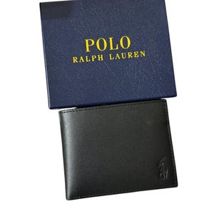 May include: Black leather wallet with a small embossed logo, presented with a navy blue box. The box features the text "POLO RALPH LAUREN" in gold lettering. The wallet is a classic bi-fold design.