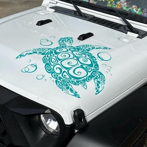 May include: A white vehicle bonnet featuring a teal sea turtle decal. The turtle design has swirling patterns and is surrounded by bubbles. The bonnet is part of a white vehicle with black detailing.