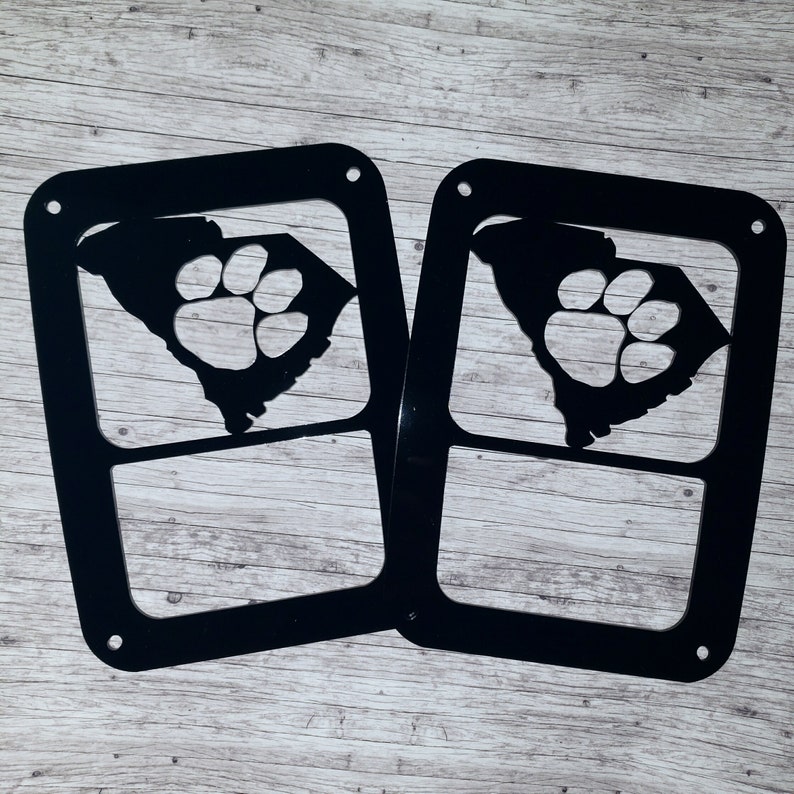 Puede incluir: Dos recortes de metal negro del estado de Carolina del Sur con una huella de pata en el interior. Los recortes est&aacute;n dise&ntilde;ados para ser utilizados como cubiertas de luz.