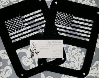 May include: Two black metal Jeep Wrangler door inserts with a cut-out American flag design. The inserts are on a gray and white patterned surface. A business card for Jeep N Jewelry is visible in the image.