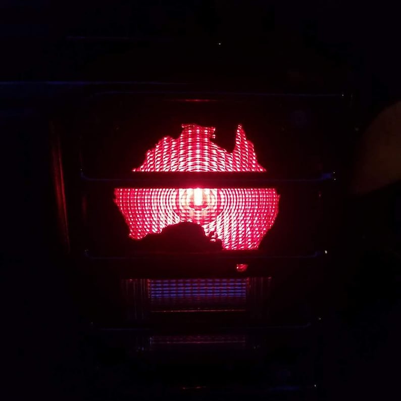 Puede incluir: Una luz roja con la forma del contorno de Australia. La luz est&aacute; iluminada y tiene un patr&oacute;n de cuadr&iacute;cula.