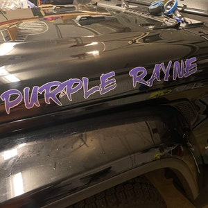 May include: A black Jeep Wrangler with a purple and white "PURPLE RAYNE" decal on the hood.