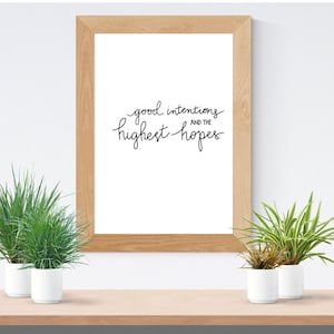May include: A framed print with the text "good intentions and the highest hopes" in black cursive writing on a white background.