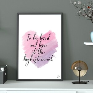 May include: A black framed print with a watercolor background in shades of pink and purple. The print features the text "To be loved and love, at the highest count".