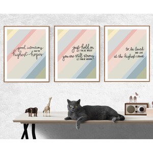May include: Three framed prints with colorful striped backgrounds and inspirational quotes. The quotes are "good intentions and the highest hopes", "just hold on let time be intent you are still strong let pain be gracious", and "to be loved and love at the highest count".