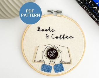 以下が含まれることがあります： 「Books & Coffee」というテキストと、開いた本の真上にコーヒーカップを持った手のイラストが描かれた刺繍のフープアートです。