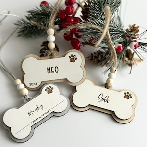 May include: Three wooden dog bone-shaped ornaments with paw prints and names "Neo", "Cola", and "Murphy". The "Murphy" ornament includes the text "Forever in Our Hearts". Each ornament has a string for hanging and decorative beads.