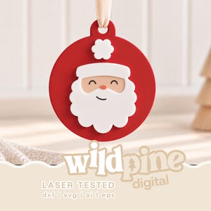 May include: A circular red ornament featuring a white Santa Claus face with a matching hat pom-pom, suspended by a light beige ribbon. The design includes the text "wildpine digital" and "LASER TESTED dxf | svg | ai | eps" at the bottom.