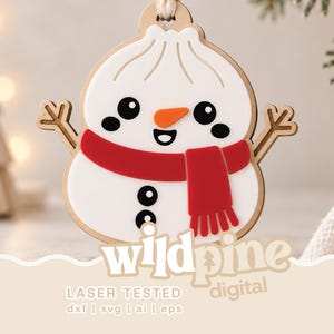 May include: A white snowman ornament with a red scarf, orange carrot nose, and black button details. The snowman has twig-like arms and a wooden border. The text "wildpine digital" and "LASER TESTED dxf | svg | ai | eps" is printed at the bottom.