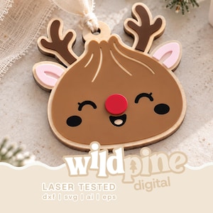 Könnte beinhalten: Ein flaches, mehrschichtiges Holzornament in Form eines Dumplings mit Rentiergeweih, roter Nase und lächelndem Gesicht. Das Design zeigt braune, rosa und rote Akzente. Der Text unten lautet wildpine digital LASER TESTED dxf | svg | ai | eps.