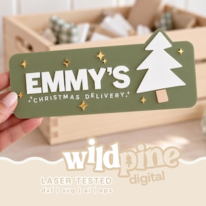 May include: A rectangular olive green sign featuring the white text EMMY'S CHRISTMAS DELIVERY, a white Christmas tree icon, and several small gold star accents. The sign has rounded corners and a smooth, flat surface with raised lettering.