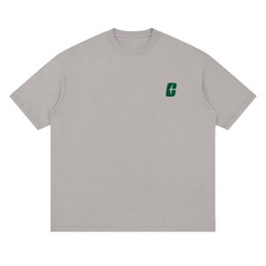 May include: A light gray t-shirt with a crew neck and short sleeves. A small green graphic is on the upper left chest. The shirt has a relaxed fit and a simple, minimalist design.