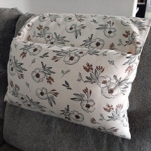 May include: A decorative pillow with a floral pattern. The pillow features a white background with a repeating design of gray and brown flowers and leaves. The pillow is rectangular and appears to be made of fabric.
