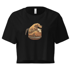 May include: Black crop top featuring a graphic of a coffee pot with a wave design in shades of brown and beige. The coffee pot has a handle and a spout. The wave design is reminiscent of Japanese art.