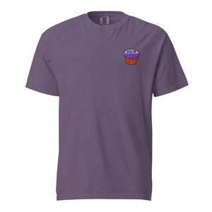 Könnte beinhalten: Ein lila T-Shirt mit einer kleinen Cupcake-Grafik auf der linken Brust. Der Cupcake hat einen lila Deckel, eine braune Basis und das Wort "POG" darüber. Das Shirt besteht aus einem weichen Material.