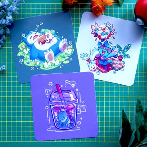 May include: Three square stickers featuring cartoon illustrations of Pokemon characters. The first sticker shows a blue and white Snorlax sleeping with a small brown Eevee. The second sticker shows a blue and white Espeon with a pink and white Sylveon. The third sticker shows a blue and white Espeon inside a purple and blue boba tea.