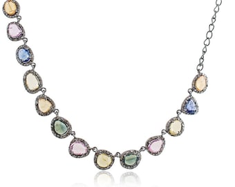 May include: A silver chain necklace with a row of colorful gemstone pendants. The gemstones are oval-shaped and have a faceted finish. The necklace is accented with small diamonds.