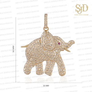 Puede incluir: Un colgante de elefante de oro con una piedra roja en la trompa. El colgante está cubierto de pequeñas piedras transparentes. El colgante mide 30 mm de alto y 35 mm de ancho.