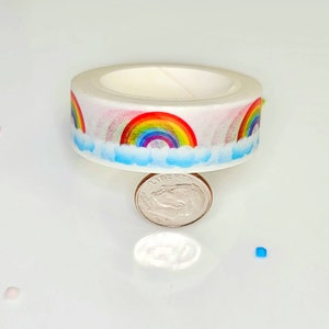 May include: A roll of white washi tape with a rainbow and cloud design. The tape is approximately the size of a UK ten pence coin.