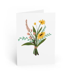 May include: A white greeting card with a floral bouquet illustration. The bouquet features yellow sunflowers, pink flowers, and green leaves, bound with pink string. The card is blank inside, ready for a personal message.