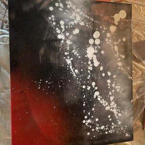 May include: Abstract art painting on canvas with a black and red gradient background and white splatter paint.