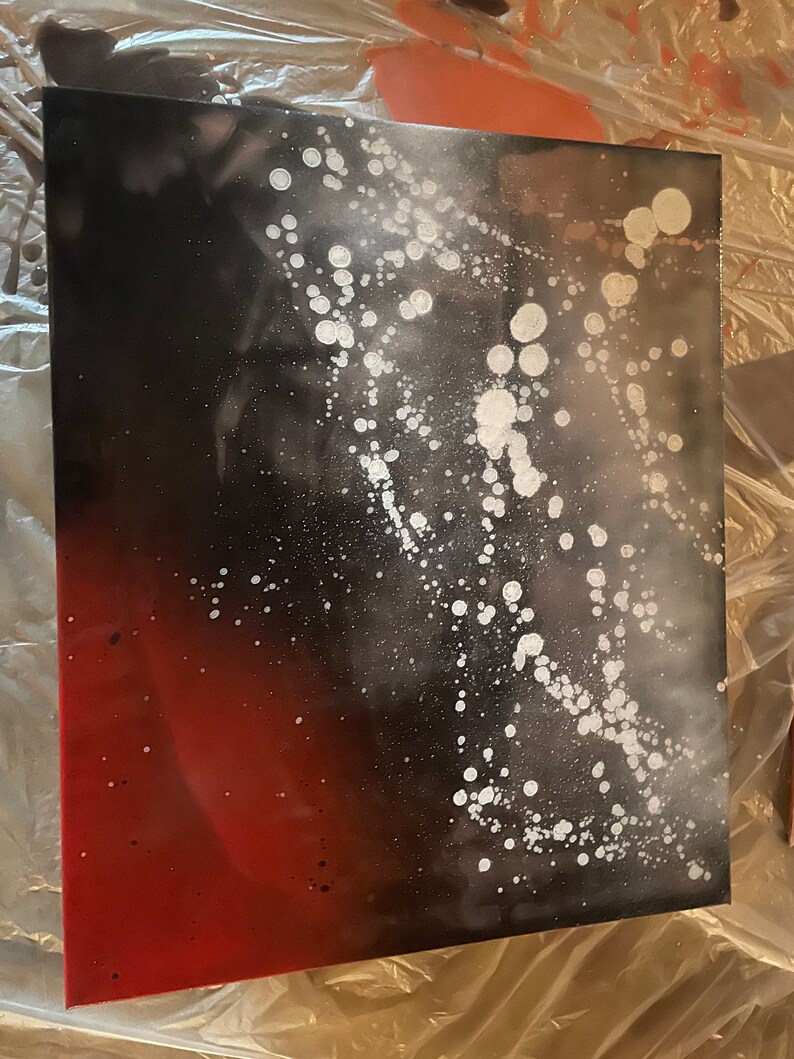 May include: Abstract art painting on canvas with a black and red gradient background and white splatter paint.